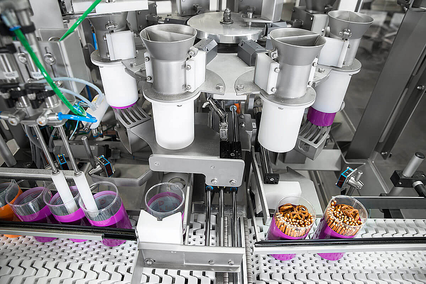Blick von oben auf Dosiermaschine, die Salzstangen und –Brezeln in Dosen verpackt