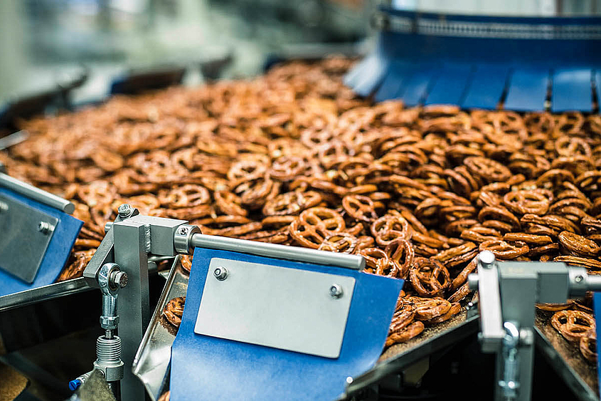 Pesadora multicabezal para aperitivos como pretzels Una pesadora multicabezal distribuye pequeños pretzels salados
