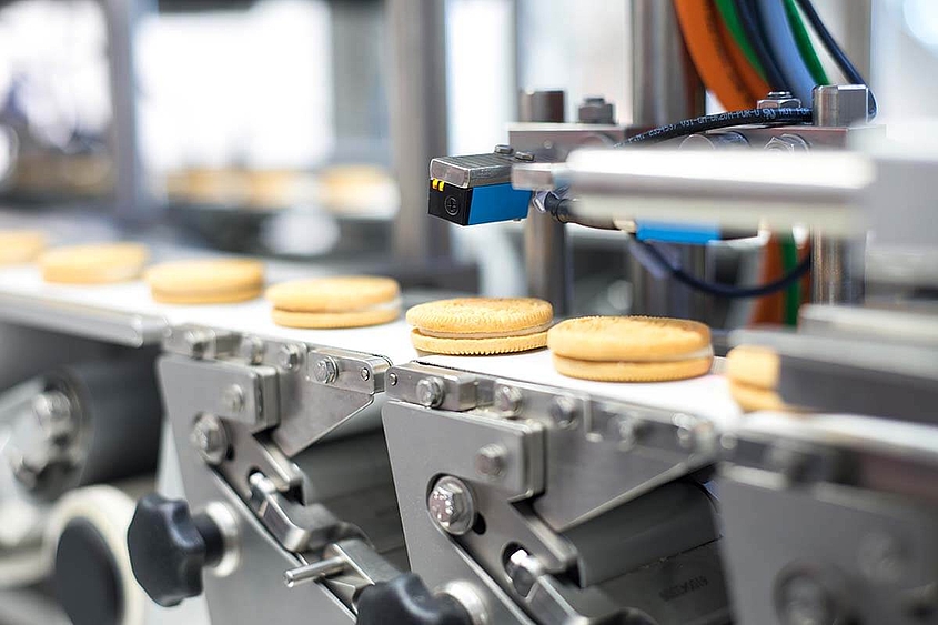 Doppelkekse mit weißer Füllung werden einzeln auf einem Förderband transportiert.