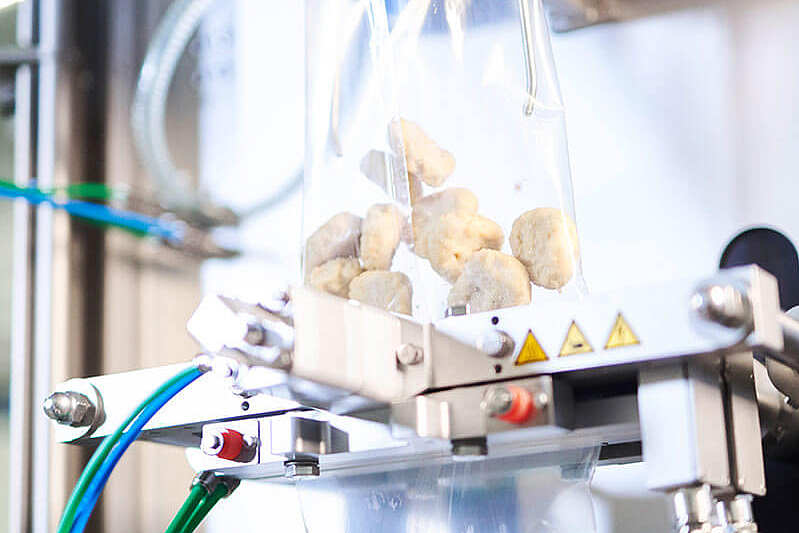 Detailansicht einer vertikalen Schlauchbeutelmaschine mit Chicken Nuggets in zwei durchsichtigen Beuteln