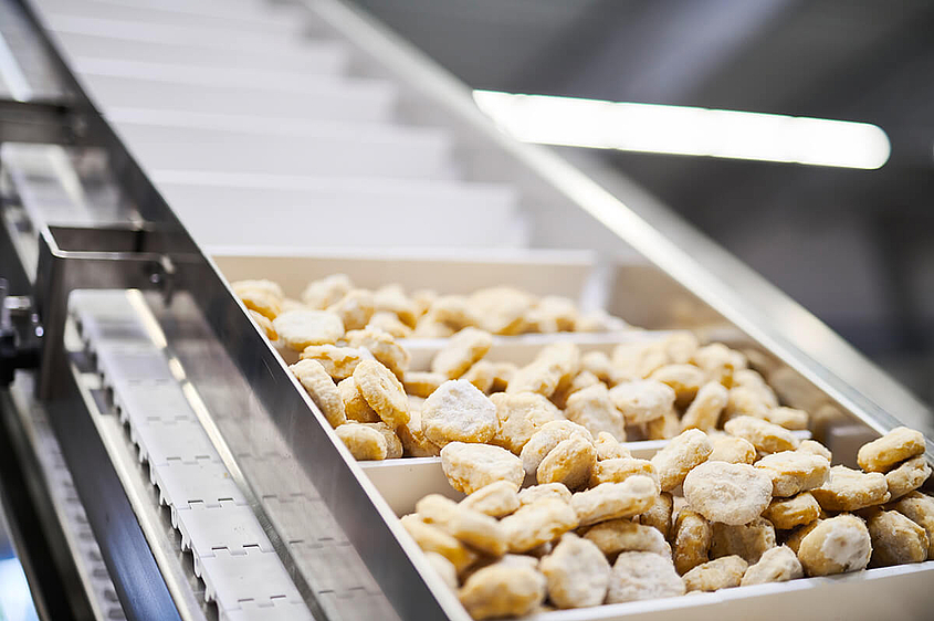 Unverpackte Lebensmittel wie Nuggets laufen über ein Fließband 